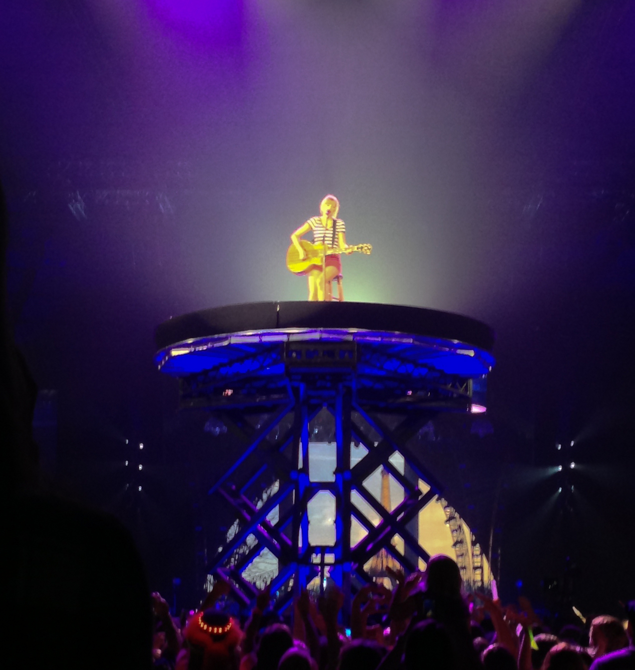Taylor Swift singing into a microphone under stage lights during a concert tour